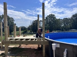 A man is working on a wooden deck project for a swimming pool.